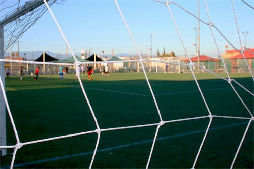 Seen through a soccer goal net, people play soccer in Debs Park.