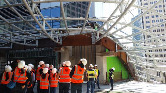 The ACE Mentor Program provides Bell students with an exclusive tour of the Wilshire Grand Center while under construction. Project Safety Manager, Abner Estrada, informs the students on the progression of construction and functionality of the tower’s technologically advanced building design. The group looks upward while spotting the details of the open-roofed entrance hall and the building’s rising floors.
