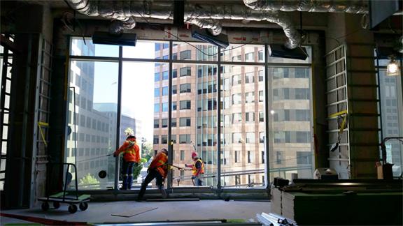 Three construction workers cooperate to put the building’s windows in place